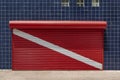 Closed store shutter painted to red scuba diving flag with a wall covered with blue tiles Royalty Free Stock Photo