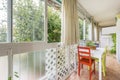 Closed terrace of a house with a white table and indoor hanging plants, white wooden latticework and views of a wooded garden Royalty Free Stock Photo