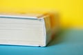 A closed thick white book or diary lies on a yellow and blue background. College or school science library. Close-up. Shallow