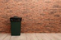 Closed trash bin near brick wall indoors, space for text. Royalty Free Stock Photo