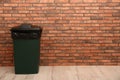 Closed trash bin near brick wall indoors, space for text. Royalty Free Stock Photo