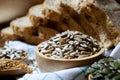 Closed up organic sunflower seeds in wooden bowl over blur whole wheat bread, golden flax and pumpkin seed on white table cloth Royalty Free Stock Photo