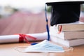 Closed-up photo of a college graduation cap mortarboard with degree diploma certificate and face mask on the table. Graduation in