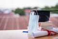 Closed-up photo of a college graduation cap mortarboard with degree diploma certificate and face mask on the table. Graduation in