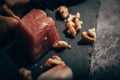 Closed up of several pieces of walnut next to a raw red beef cube on a black slate