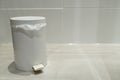 A closed white pedal bin standing on a tiled floor in a bathroom, concept for tidiness and environment
