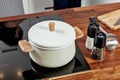 Closed white saucepan with wood pens on the black stove and glass spice mills with papper and salt on the wood table in the Royalty Free Stock Photo