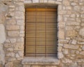 Closed window with wooden shutters and bars with a stone window sill in the old wall of the house Royalty Free Stock Photo