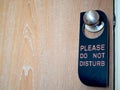 Closed wooden door of hotel room with please do not disturb sign hanging on the stainless steel door knob Royalty Free Stock Photo