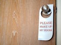 Closed wooden door of hotel room with please make up my room sign hanging on the stainless steel door knob