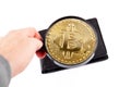 Closer look at a crypto currency wallet, hand holding a loupe revealing a golden bitcoin coin inside. Cryptocurrency storing