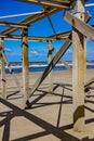 Closeup of abandoned structure with wooden posts and beams on the beach with the sea with small waves and foam in the background