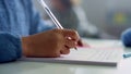 Girl writing in notebook at desk in classroom. Student doing classwork at school