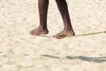 Closeup African American man feet walking on tightrope or slackline on sandy background. Slacklining is a practice in