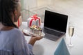 Closeup of african american woman holding birthday cake, using laptop