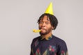 Closeup african man with dreadlocks wearing party cone cap and blowing party pipe, celebrating anniversary, hungout