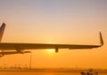 Closeup airplane wing with golden sunrise sky. Plane parked at airfield of airport. Morning flight. Summer travel concept.