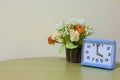 Closeup alarm blue clock, 4 o`clock with flower on wall background