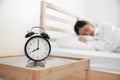 Closeup alarm clock with sleeping woman in bed room. Lazy time in holiday concept