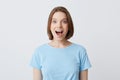 Closeup of amazed excited young woman with opened mouth in blue t shirt looks happy and shouting isolated over white background