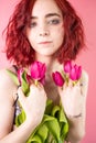 Young red head girl with flowers tulips in hands on a pink background. Royalty Free Stock Photo