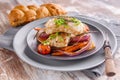 Closeup appetizing cod filet with red onion and herbs, baked potatoes and carrots on a side dish in a gray plate on a napkin.