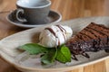 Closeup of appetizing slice of dark chocolate cake with ice cream and out of focus coffee cup in background