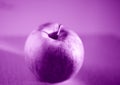 Closeup of an apple on a table under the lights with a blurry background and a purple effect Royalty Free Stock Photo