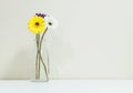 Closeup artificial colorful flower on transparent glass bottle on blurred white wood desk and cream color wallpaper at the wall