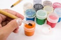 Closeup of artist hands holding wooden brush with gouache. Brush in hand and jars with gouache
