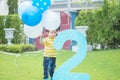 Closeup happy asian kid stand with balloon in his hand on grass floor in park textured background in 2 nd years anniversary concep Royalty Free Stock Photo