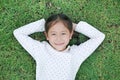 Closeup Asian little child girl smiling with hands behind head and open eyes resting on green grass outdoors in summer park. Top Royalty Free Stock Photo