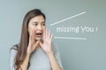 Closeup asian woman in shout action with missing you word on blurred cement wall textured background with copy space Royalty Free Stock Photo