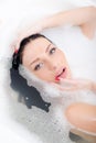 Closeup on attractive beautiful young woman with blue eyes red manicure relaxing sensually lying in spa foam bath