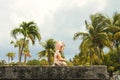 Closeup of baby angel statue kneeling on a grave with tall palm trees defocused behind