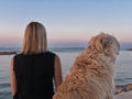 Closeup from the back of a Caucasian woman sitting by the sea with her dog watching the sunrise Royalty Free Stock Photo