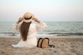 Closeup back view of woman sitting in white dress and hat looking out towards blue ocean and sky, isolated sea background Royalty Free Stock Photo