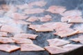 Closeup of bacon cooking on a barbecue hotplate with sizzling smoke