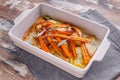 Closeup baked sliced potatoes and carrots with red onions and herbs: sage, rosemary and thyme in a ceramic baking dish