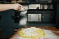 Closeup baker hands sprinkling flour on raw dough for bread