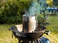 Closeup of a barbecue charcoal chimney starter on a black tripod swivel grill Royalty Free Stock Photo