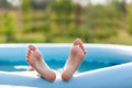 Closeup of bare feet sprinkled water, sticking out of an inflatable pool in nature. Child staying cool in the summer heat Royalty Free Stock Photo