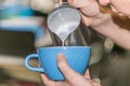 Closeup Barista in preparing proper cappuccino pouring milk froth in a cup