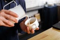 Closeup of barmen pouring milk to cappuccino cup