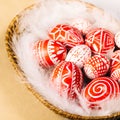 Closeup basket with Easter red eggs with folk white pattern lay on feather on vintage paper. Ukrainian traditional eggs