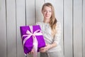 Closeup beautiful blond girl shows at camera large purple gift box holding in hands