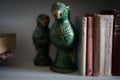 Closeup of a beautiful ceramic parrot statue on a white bookshelf next to old books