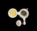Closeup beautiful ceramic tea pot with dried tea leaves on tea strainer and brown tea in a cup of tea isolated on black background Royalty Free Stock Photo