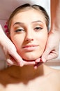 Closeup on beautiful nice young woman on spa treatments during face massage, relaxing & looking at camera