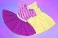 Closeup of a beautiful pink and a yellow sleeveless baby girl dress lying flat from above on an abstract light blue pink Royalty Free Stock Photo